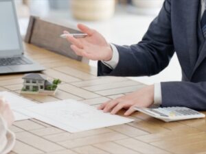 住宅模型と電卓を前に説明するスーツの営業担当者